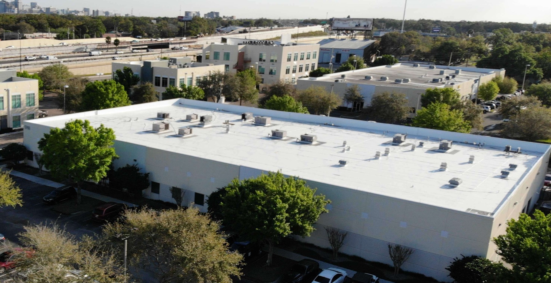 Completed white TPO single-ply flat roof on a commercial building beside I-4 in Orlando, with the downtown skyline behind